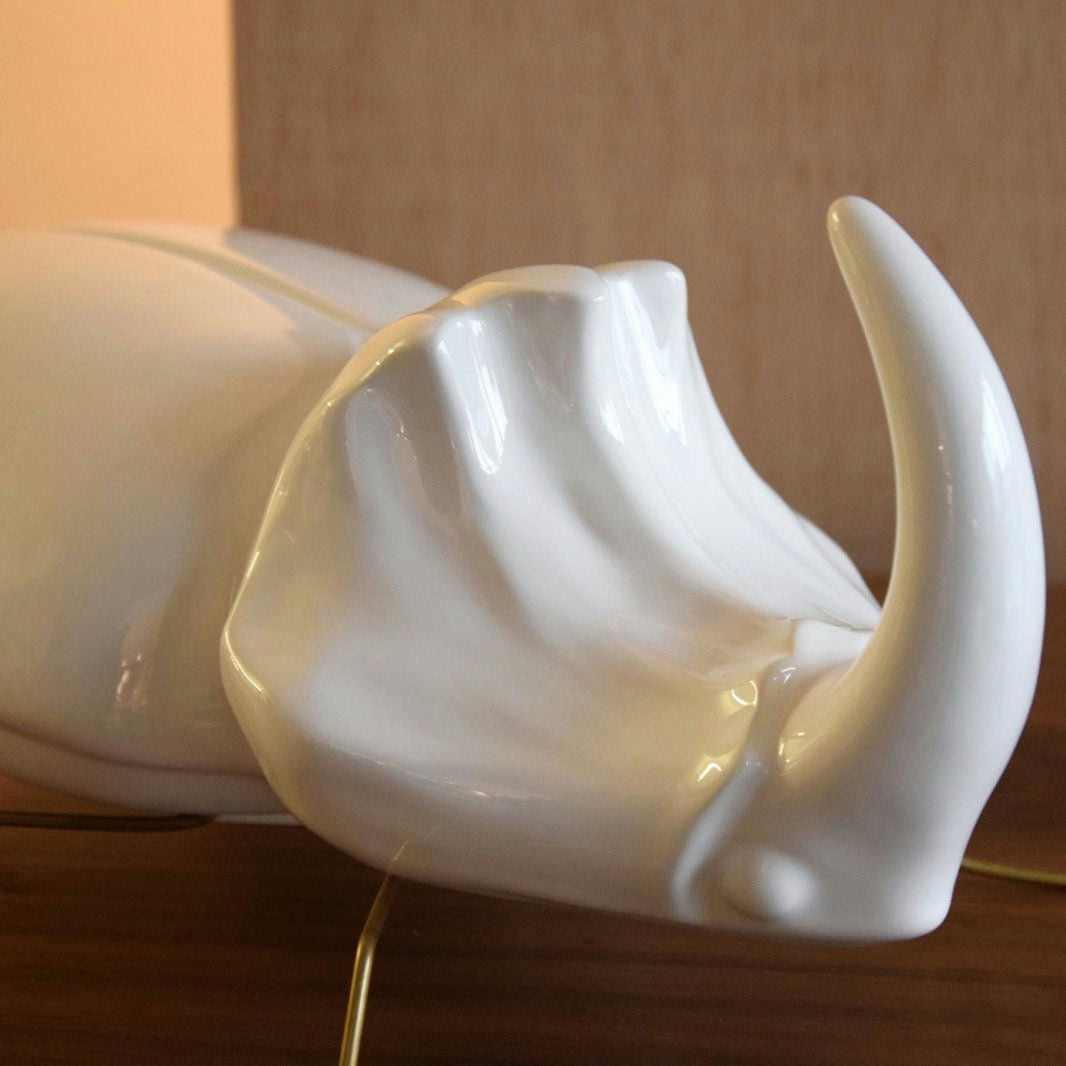 Primer plano de un elegante montaje con la Escultura Cerámica Escaravello Corno Blanco Brillo, una escultura de cerámica que se asemeja a una cabeza de rinoceronte, colocada sobre una superficie de madera.