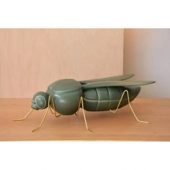 Una Escultura Cerámica Mosquito - Verde Militar Mate sentada sobre una mesa de madera, agregando un toque de decoración verde militar mate.