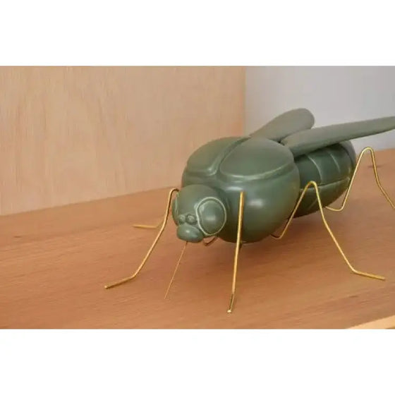 Descripción: Una Escultura Cerámica Mosquito - Verde Militar Mate decorando una repisa de madera.