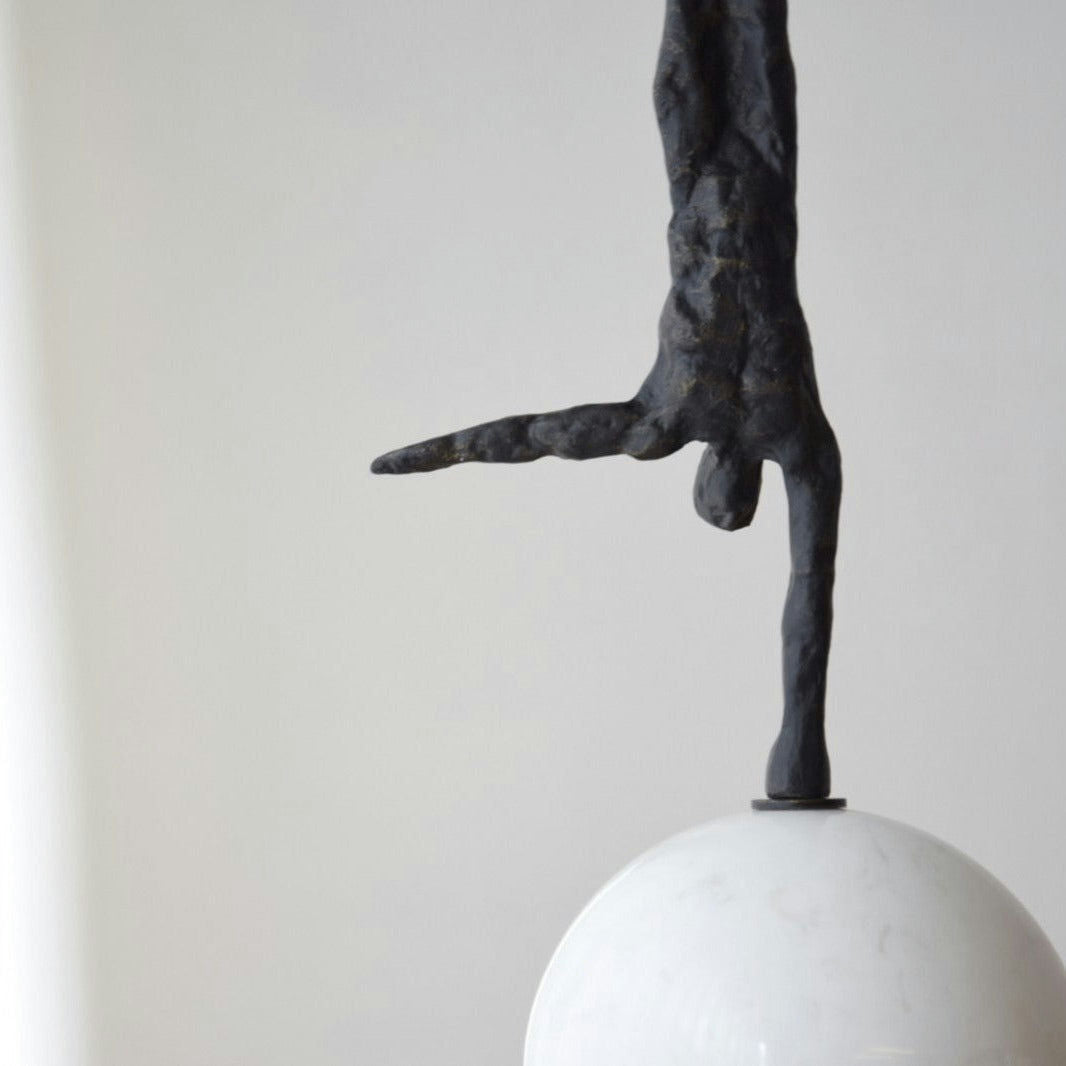 La Escultura Equilibrio N2: Metal y Mármol es una pieza minimalista que presenta una figura en equilibrio sobre una mano sobre una esfera blanca y lisa sobre un fondo claro, encarnando el arte del diseño contemporáneo.
