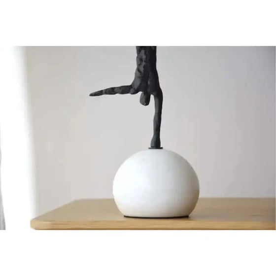 Una escultura Equilibrio N2: Metal y Mármol de una mano sobre una bola blanca.