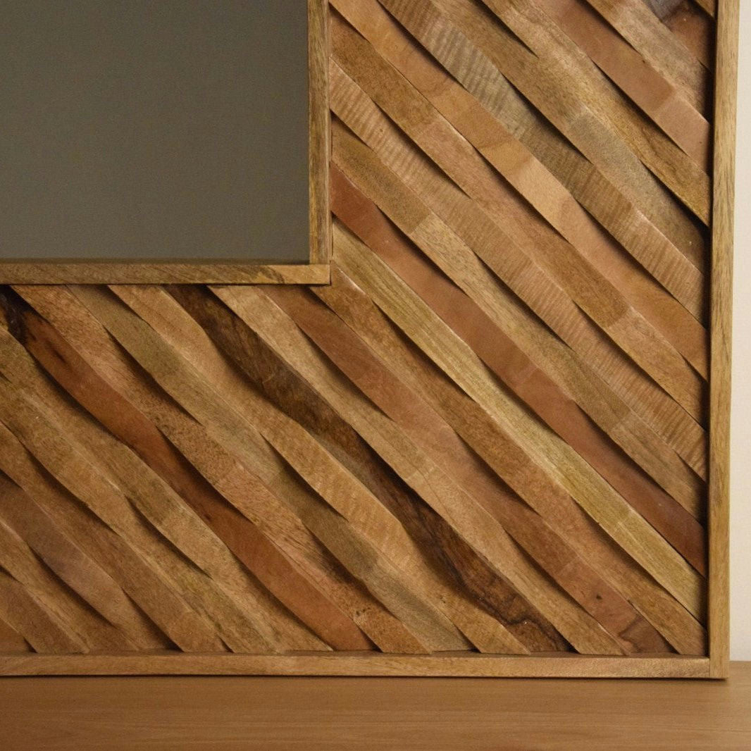 Una pared de madera con lamas diagonales complementa un "Espejo Madera Cuadrado - Quadratum" rectangular sobre un piso de madera, incorporando diseño contemporáneo y artesanía de calidad.