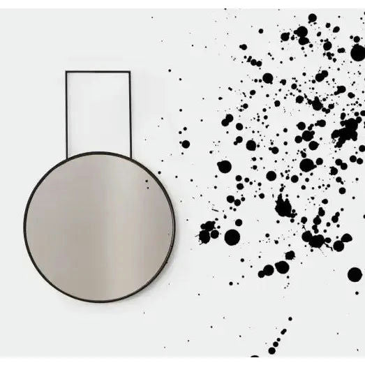El Espejo One Eyed es un espejo de pared redondo con marco negro y patrón de salpicaduras negras sobre blanco, que muestra un diseño moderno e interiores minimalistas.