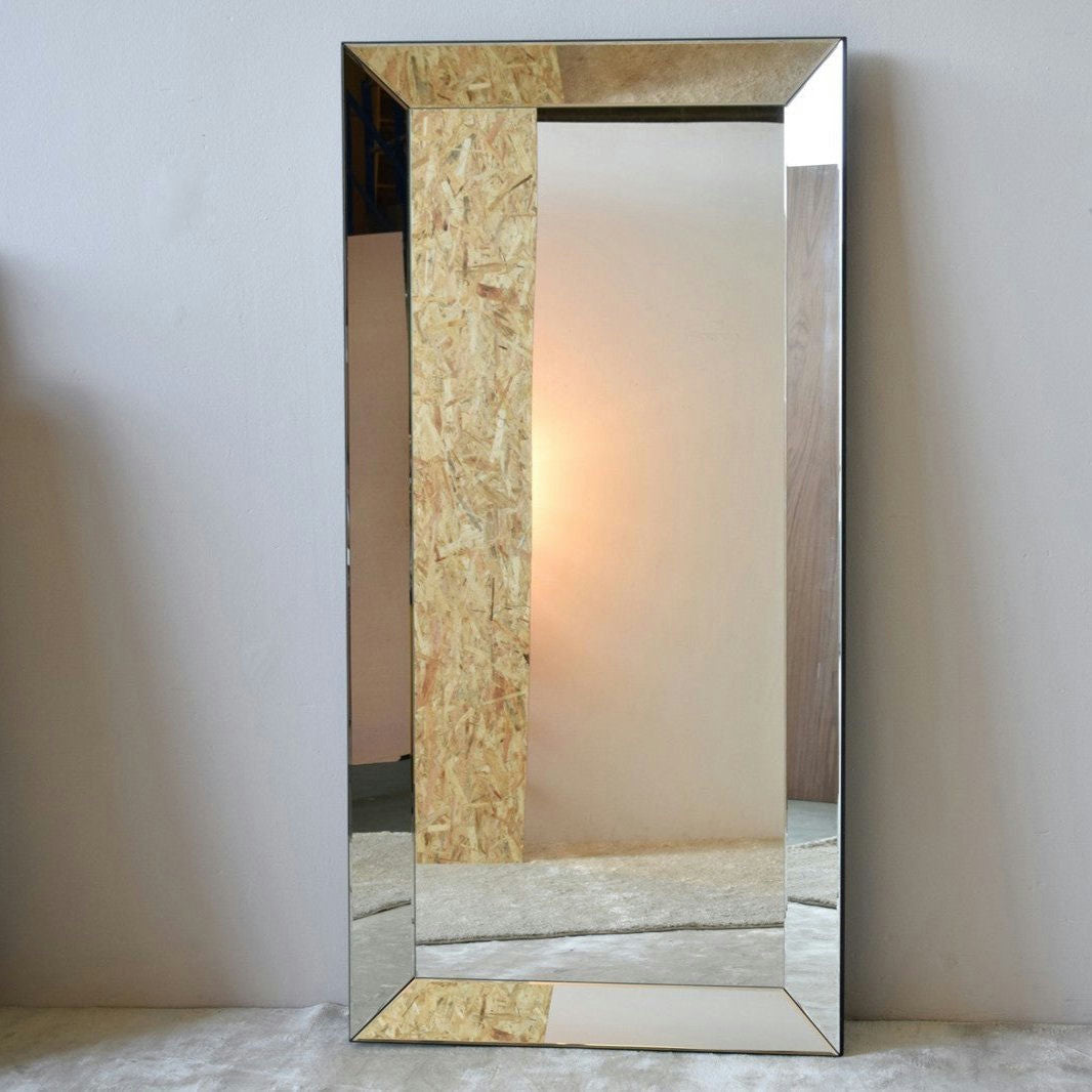 El Espejo de Suelo Rectangular - Piezas tiene un marco grueso y decorativo con un acabado con textura de madera. Refleja gradientes de luz cálidos y difusos de lámparas o ventanas en paredes lisas, agregando elegancia a cualquier habitación con su diseño contemporáneo.