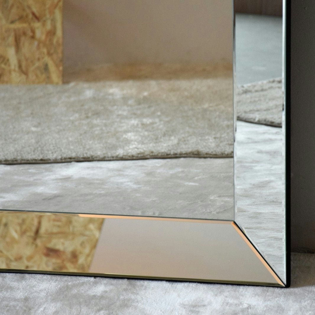 Primer plano del Espejo de Suelo Rectangular - Piezas con borde biselado, que refleja las texturas de la alfombra y la pared de madera cercanas. Su diseño contemporáneo realza la estética general.