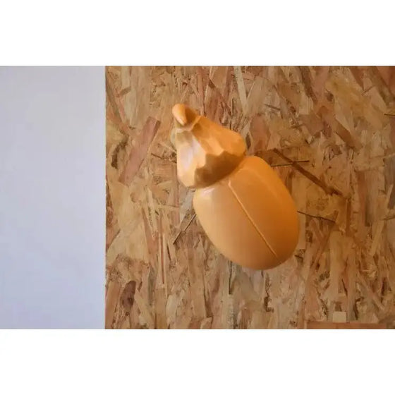 Una Figura Cerámica Escaravello Corno Mostaza Mate con un elegante encanto rústico apoyada en una pared de madera.