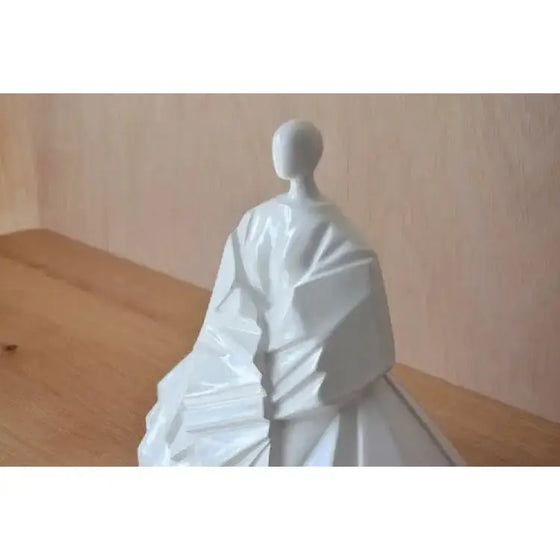 Una Figura Cerámica Japonesa Manga Extendida Blanco Brillo de una mujer con un vestido sobre una mesa de madera, inspirada en el arte cerámico japonés.