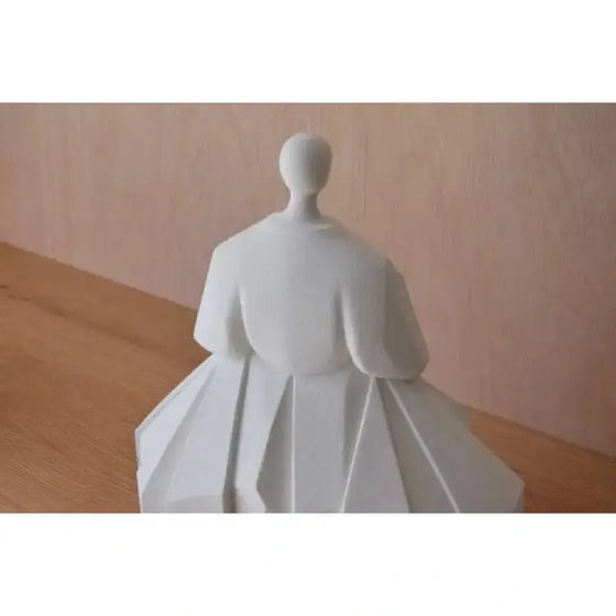 Una Figura Cerámica Japonesa Manga Extendida Blanco Mate de una mujer sentada sobre una mesa de madera, que muestra el arte cerámico tradicional.