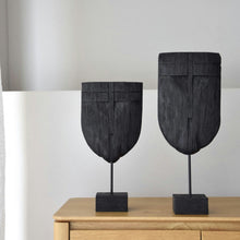  Dos esculturas abstractas de madera negra de la colección Figura decorativa en madera de mango Máscara descansan elegantemente sobre un mueble contra una pared de color claro. Cada pieza aporta intriga, fusionando de forma hermosa la artesanía tradicional con el diseño moderno.