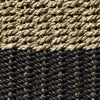 Primer plano de fibras entrelazadas en el Puff de seagrass negro y natural Black/Nat 33x46: fibras de color marrón claro en la parte superior y gris oscuro en la parte inferior, mostrando un tejido intrincado que combina calidad artesanal con diseño moderno.