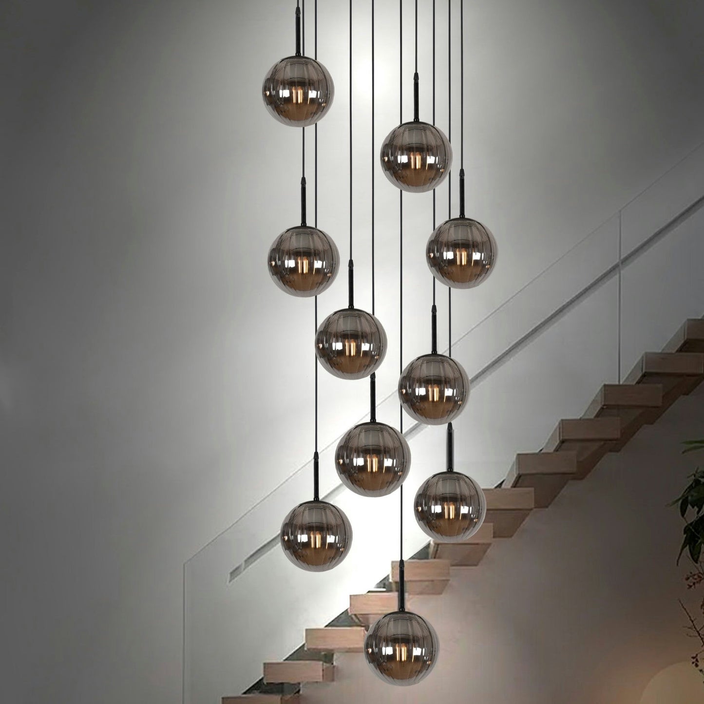 La Lámpara De Techo Colgante Moderna 168-10C-19, con esferas de vidrio ahumado, cuelga en formación escalonada sobre una escalera moderna con barandilla de vidrio, proporcionando una sorprendente iluminación moderna.