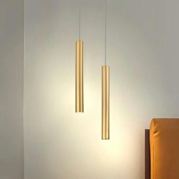 La Lámpara de Techo Colgante Duo Dorada 3048-2R proyecta un brillo cálido en una pared beige junto a una silla tapizada en naranja, con su diseño moderno y llamativos acabados metálicos que combinan elegancia y funcionalidad.