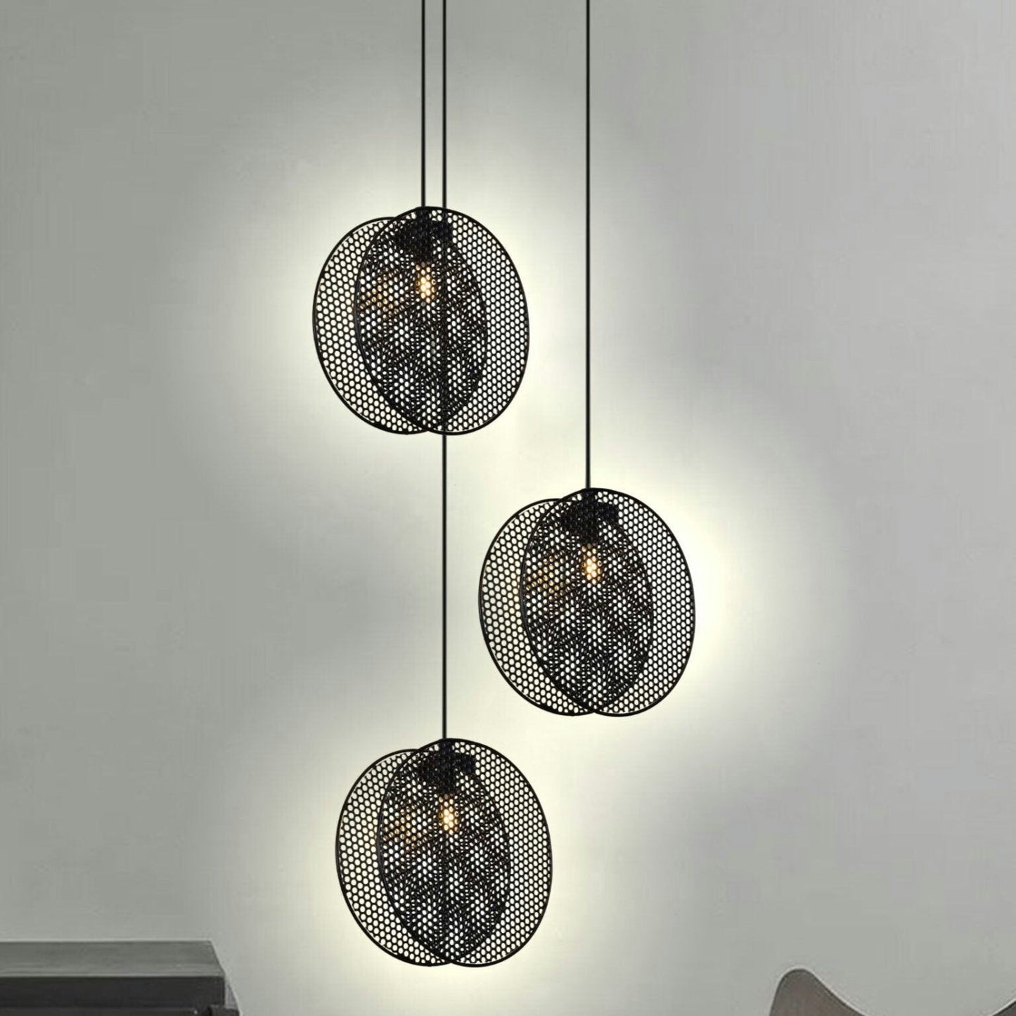 La Lámpara de Techo Colgante Moderna 3224-3C-1 Negra, con un diseño perforado, cuelga elegantemente sobre una pared de color claro. Su estilo industrial chic proyecta una iluminación suave en toda la habitación.