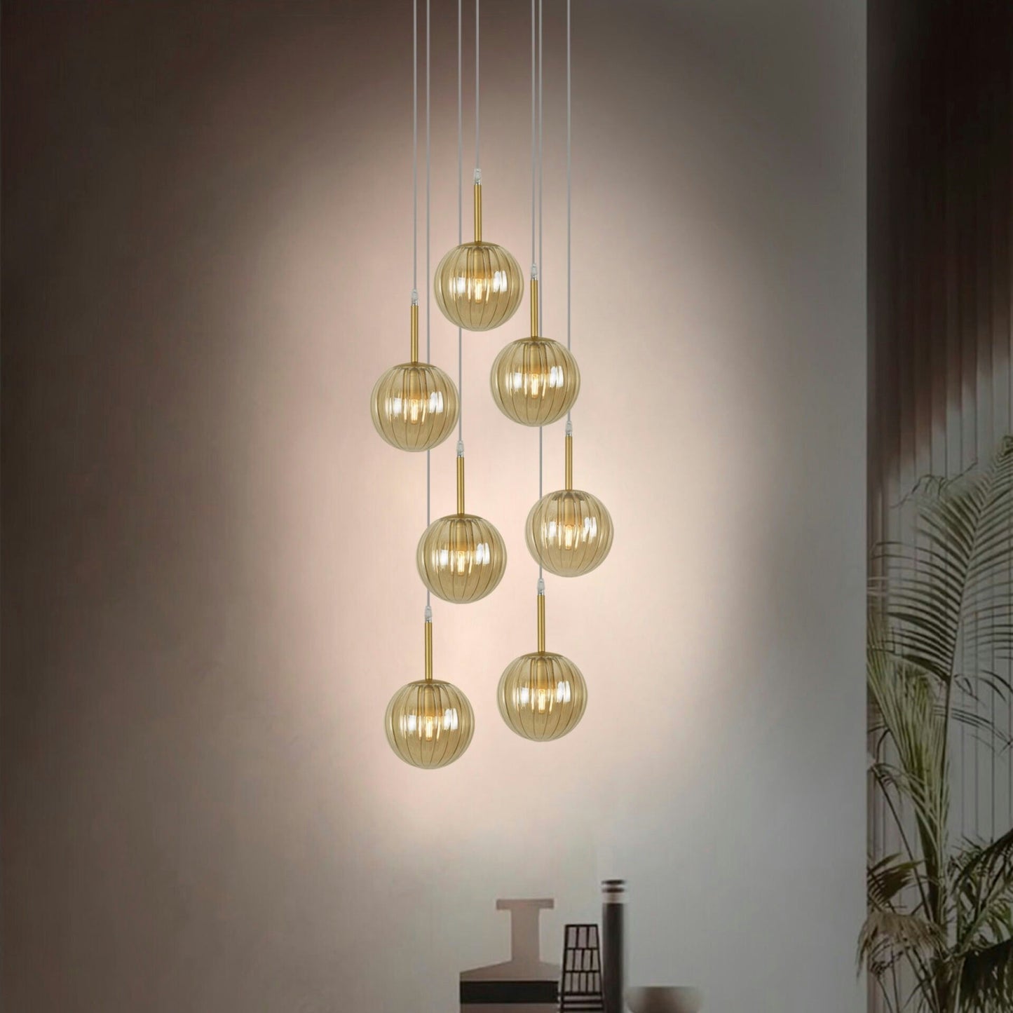 La Lámpara de Techo Colgante Moderna Cristal 168-7C, con siete luces colgantes modernas con esferas doradas y accesorios cilíndricos dorados, ilumina una habitación poco iluminada con una iluminación cálida.