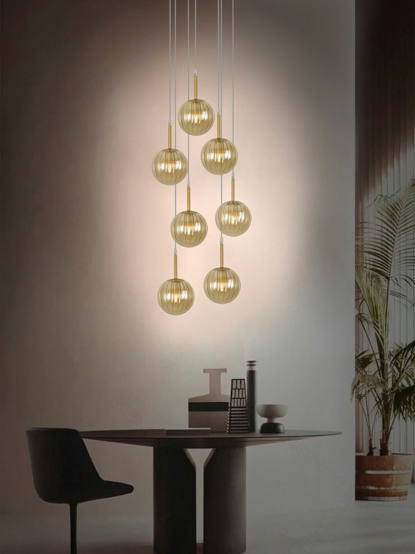 Un comedor moderno cuenta con una mesa redonda oscura, sillas negras y la Lámpara de Techo Colgante Moderna Cristal 168-7C con esferas doradas. Una planta en maceta en el fondo agrega naturaleza a la escena acogedora, realzada por una iluminación cálida.