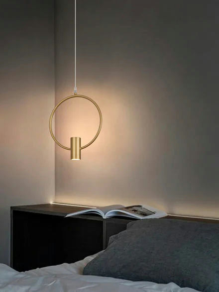 La Lámpara de Techo Colgante Moderna Dorada 6902-1C cuelga sobre una cama con una almohada gris y un libro abierto en la cabecera de madera oscura, añadiendo sofisticación y elegancia.