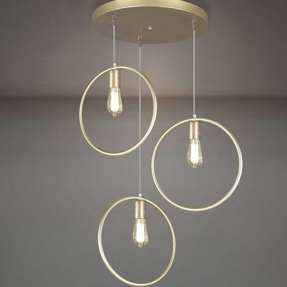 La Lámpara de Techo Colgante Moderna Oro 3134-3C cuenta con tres bombillas colgantes dentro de marcos metálicos circulares. Su elegante acabado dorado sobre un fondo gris aporta un ambiente elegante y sofisticado con un diseño contemporáneo.