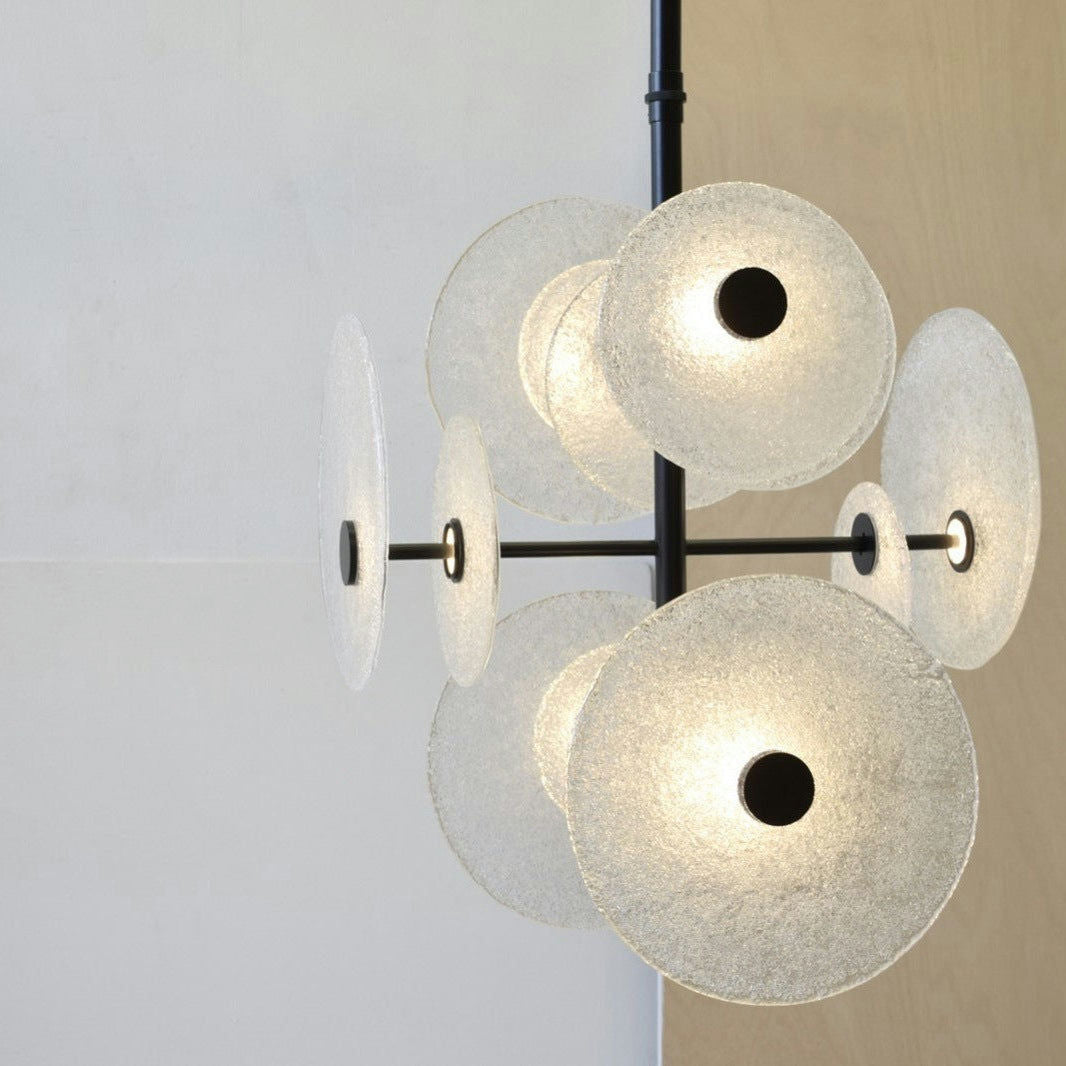La Lámpara de Techo LED de Vidrio y Metal - Discos presenta discos circulares de vidrio esmerilado y casquillos de luz negros, que cuelgan elegantemente contra una pared de dos tonos, personificando el diseño moderno en iluminación decorativa.