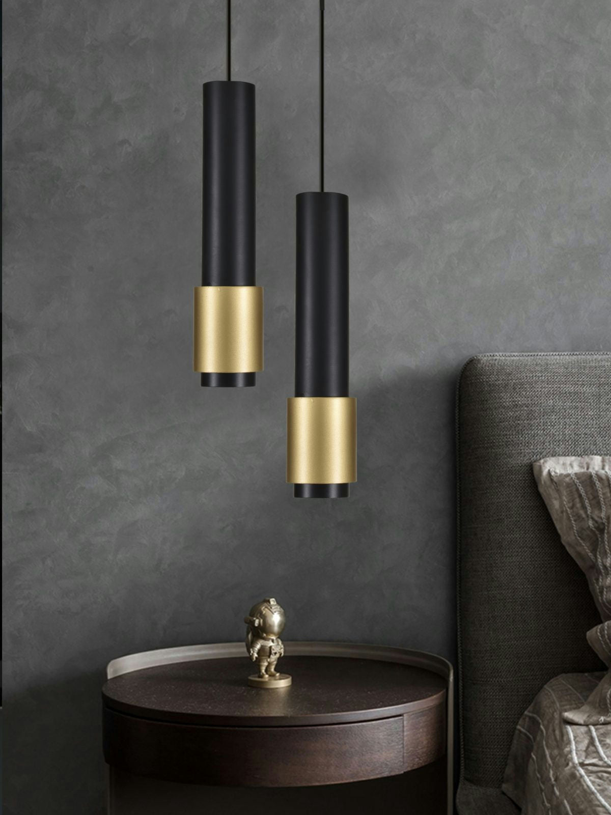 Dos lámparas de techo modelo 3044, modernas y elegantes, acabadas en oro y negro, cuelgan sobre una mesa auxiliar redonda de madera junto a una cama tapizada en gris.