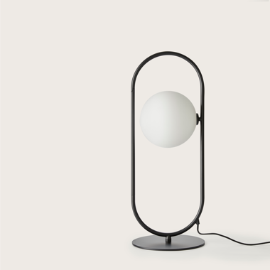 La lámpara de mesa Abbacus presenta un diseño contemporáneo con un marco circular de metal negro y una bombilla esférica blanca central sobre una base redonda, integrando elegantemente elementos de acero y vidrio soplado, ya que su cable de alimentación se extiende sin problemas desde la base.