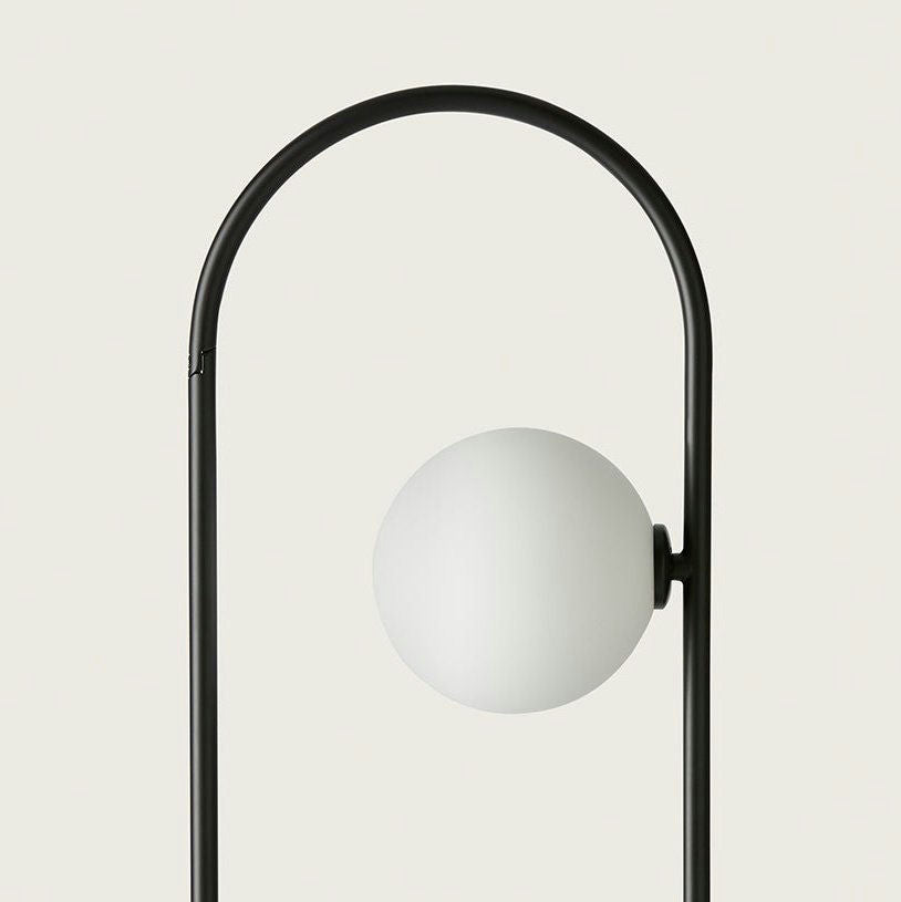 La minimalista Lámpara de Mesa Abbacus presenta un marco arqueado negro hecho de acero y vidrio soplado, complementado por una lámpara esférica blanca sobre un fondo claro.