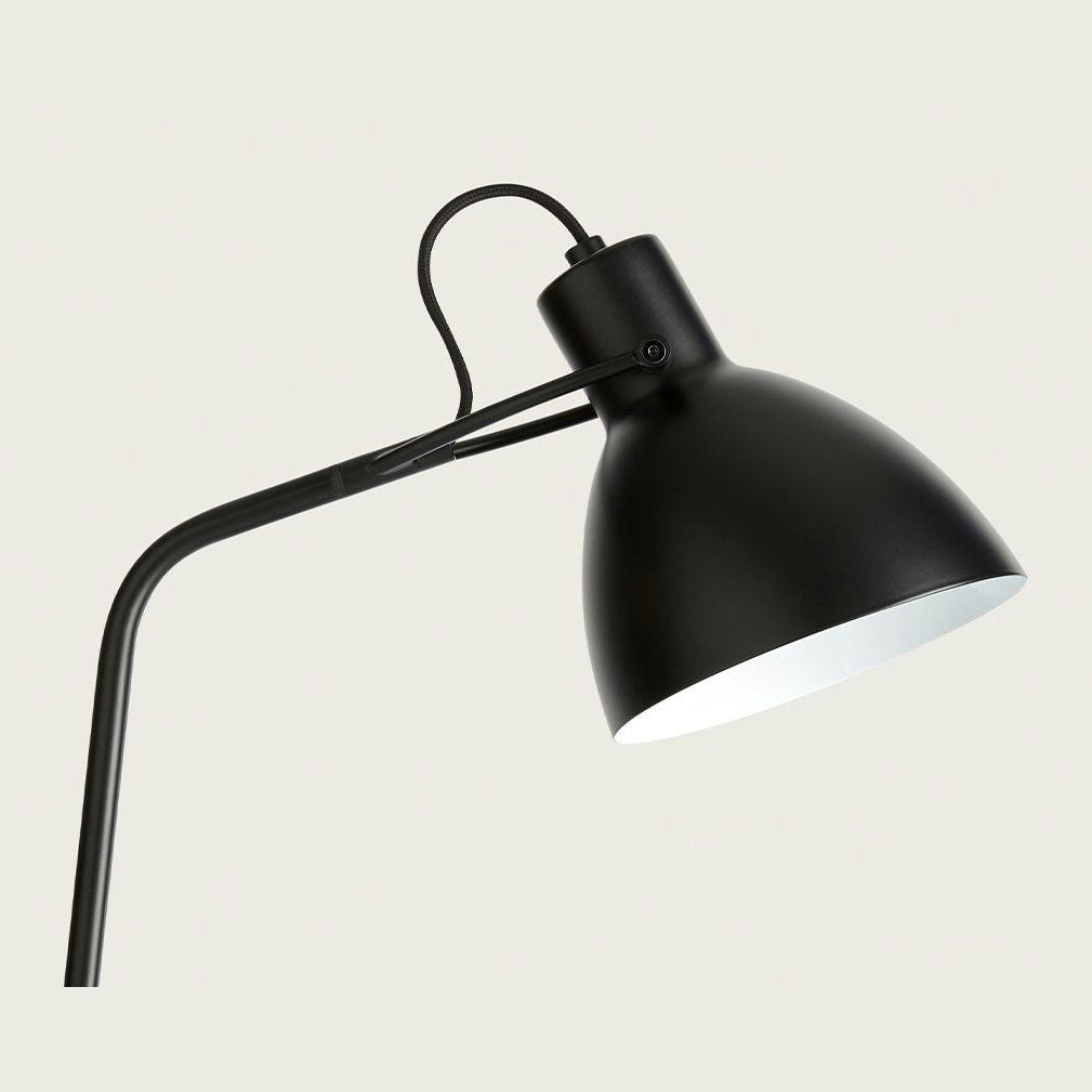 La lámpara de mesa Aito, con un elegante diseño de metal negro con un brazo curvo y una pantalla redonda, ejemplifica el diseño industrial sobre un fondo gris claro.