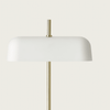 Una lámpara de mesa moderna con pantalla blanca en forma de cúpula con tecnología LED y un esbelto soporte vertical dorado, sobre un fondo liso y claro.