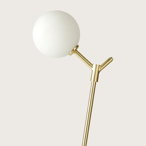 Una moderna lámpara de pie dorada Lámpara de mesa Atom con una pantalla esférica blanca montada sobre una estructura metálica elegante y ramificada sobre un fondo liso, que ofrece una iluminación suave y cálida.