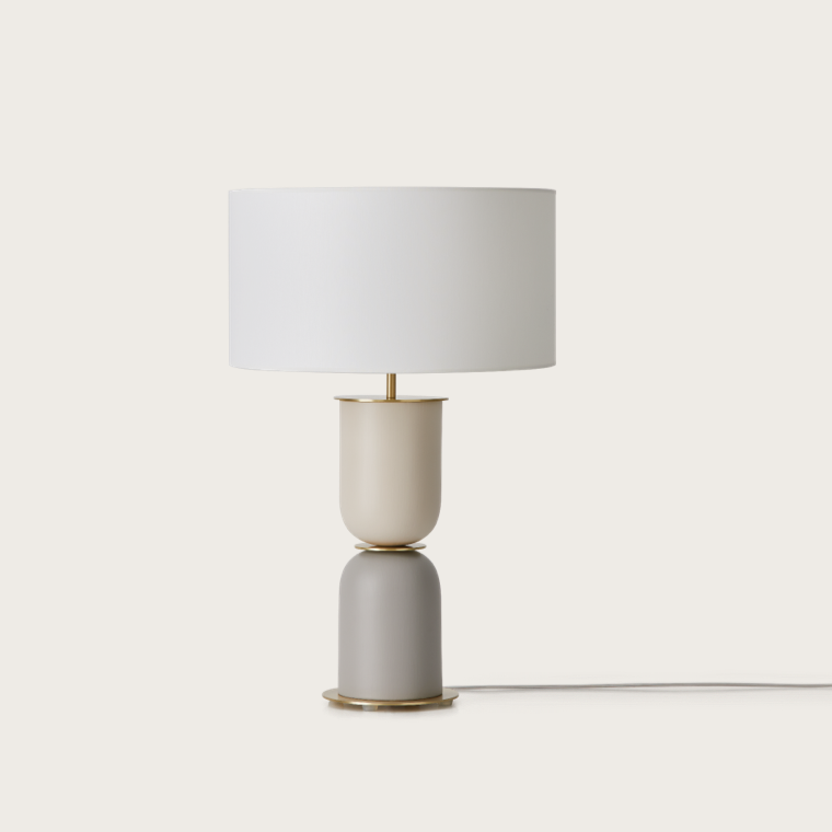 La lámpara de mesa Copo presenta una pantalla cilíndrica blanca y una base apilada de dos tonos en beige y gris, ofreciendo un toque elegante y sofisticado a cualquier habitación con su diseño contemporáneo.