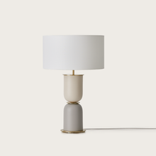  Una lámpara de mesa moderna, Lámpara de mesa Copo, con una base cilíndrica en color beige y gris y una pantalla blanca nítida, diseñada para iluminación interior, aislada sobre un fondo blanco.
