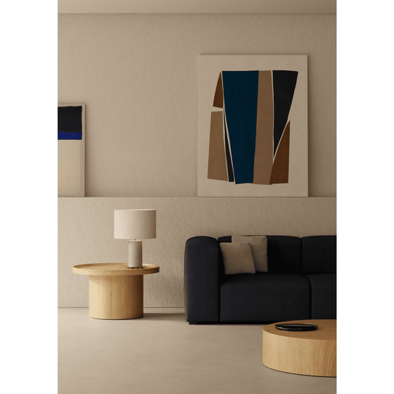 Rincón de salón moderno con un sofá azul marino, una mesa de centro redonda de madera, una lámpara de mesa Dab blanca y un cuadro abstracto en una pared beige.