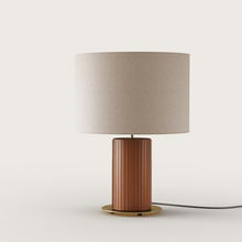  Lámpara de mesa Dab con una pantalla cilíndrica beige y una base de bronce texturizada sobre un fondo blanco.