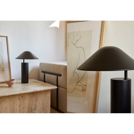 Dos Lámpara de mesa Damo negra con pantallas redondeadas sobre un escritorio moderno, junto a obras de arte enmarcadas y un sofá beige en una habitación bien iluminada, con diseño contemporáneo.