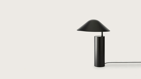 Una lámpara de mesa Damo negra con una pantalla cónica y base cilíndrica, ambientada en un fondo blanco.