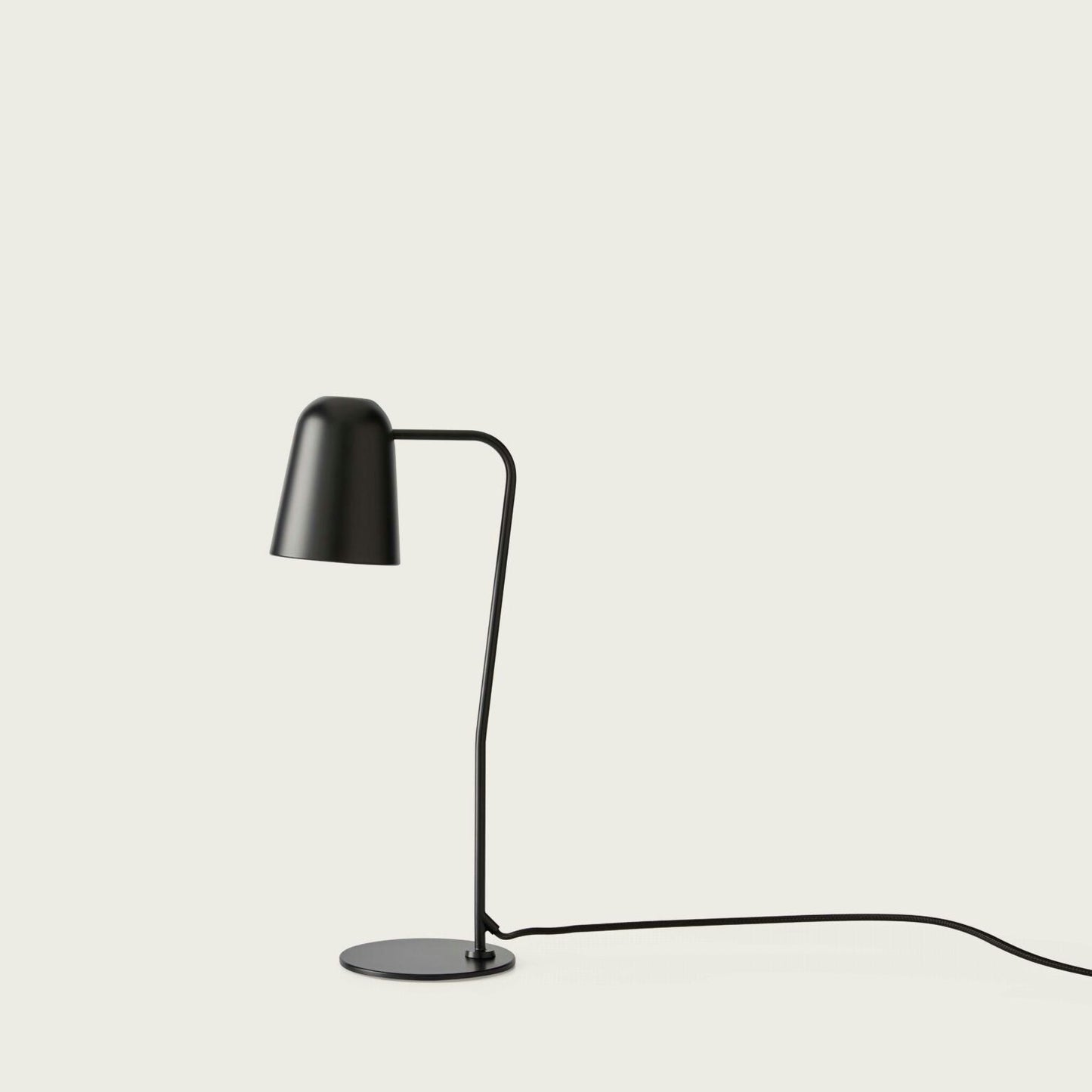 La Lámpara de mesa Dobi es una lámpara de escritorio minimalista de color negro con brazo curvo y base circular, ideal para una iluminación dirigida sobre un fondo de luz lisa.