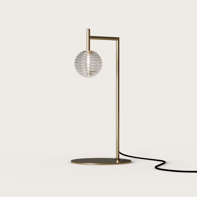 La Lámpara de Mesa Doul cuenta con un marco de latón y una pantalla de vidrio estriado que refleja un diseño contemporáneo. Descansa sobre una base redonda con un cable de alimentación negro, lo que proporciona una iluminación adaptable a cualquier espacio.