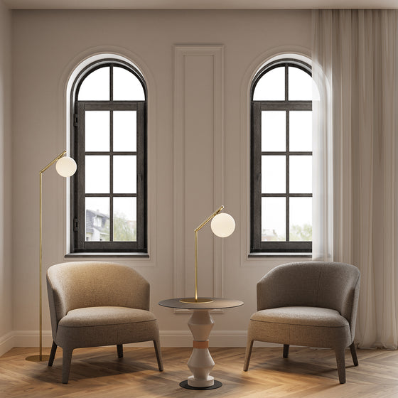 Dos elegantes ventanas en forma de arco flanquean una sencilla mesa auxiliar rodeada por dos sillas tapizadas y lámparas Lámpara de mesa Endo con iluminación ajustable en una habitación serena.