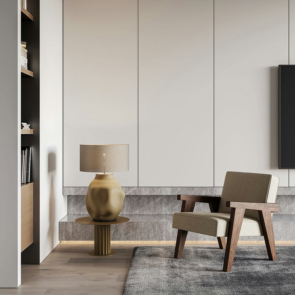 Sala de estar minimalista moderna con un sillón beige, una mesa auxiliar redonda con una elegante lámpara de mesa Etho, paneles de pared grises texturizados y estanterías empotradas con libros. Esta elegante disposición refleja una exquisita decoración de interiores.