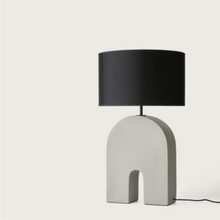  Una moderna Lámpara de mesa Home con un tono oscuro y una base metálica única en forma de arco, aislada sobre un fondo blanco.