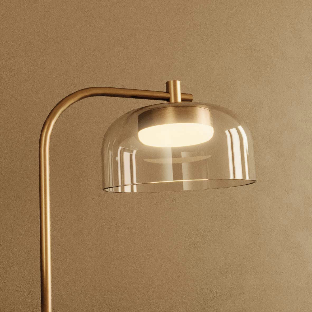 La Lámpara de mesa Ipon, con base de latón con vástago curvado y pantalla de vidrio transparente, destaca sobre un fondo beige, encarnando la elegancia minimalista.
