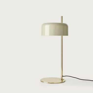 La lámpara de mesa Lalu cuenta con un diseño dorado minimalista con una base redonda, una pantalla crema brillante y un cable negro que se extiende desde la base, ideal para personalizar la iluminación para que combine con su estilo moderno.