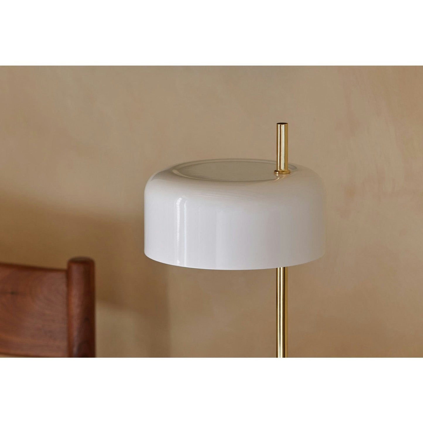 La Lámpara de Mesa Lalu, con su pantalla blanca sobre un soporte de latón, complementa elegantemente la silla de madera contra una pared beige. Es perfecta para quienes aprecian el diseño moderno y desean personalizar su espacio de iluminación.