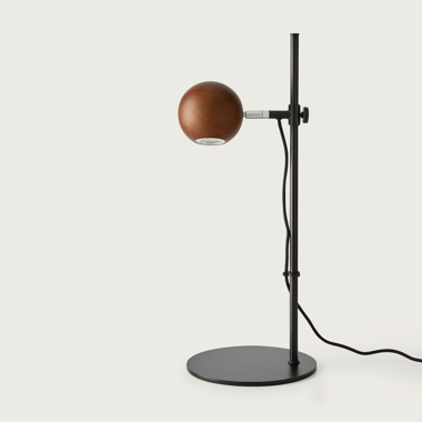 La lámpara de mesa Lita presenta una pantalla esférica de madera sobre un soporte y una base de metal negro, con un cordón negro. Este diseño moderno ofrece iluminación focalizada, ideal para cualquier entorno contemporáneo.
