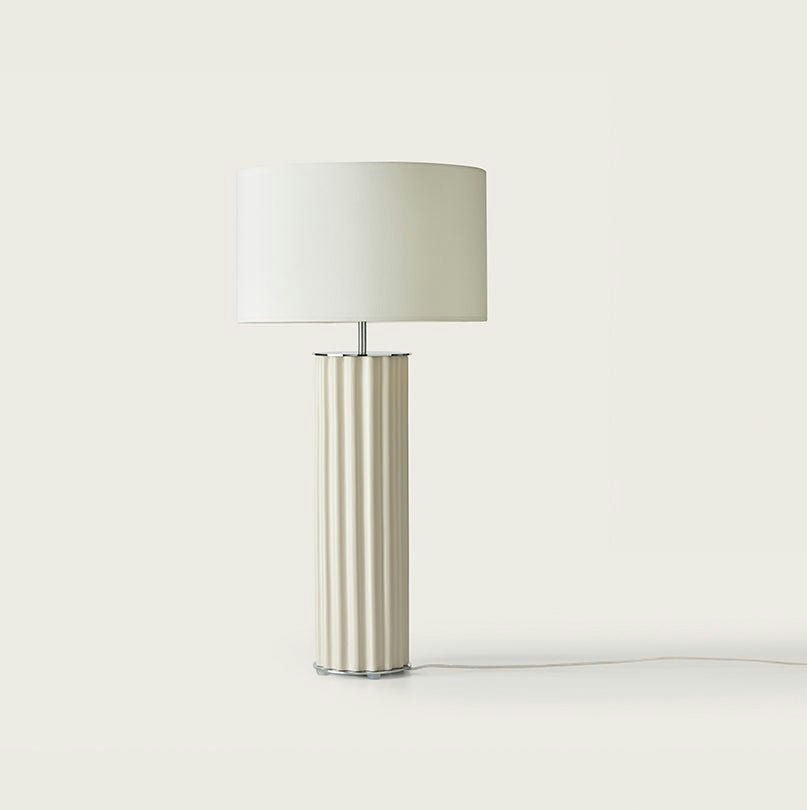 La lámpara de mesa Onica presenta una pantalla cilíndrica blanca y una base de columna vertical texturizada, que encarna el minimalismo moderno sobre un fondo claro.