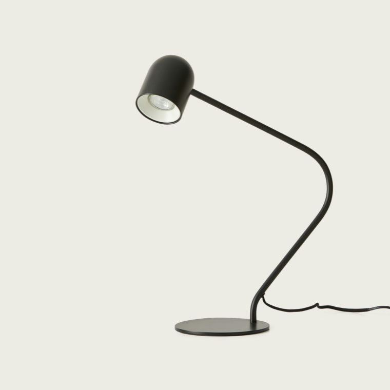 La lámpara de mesa Pipe presenta un diseño moderno en negro con líneas elegantes y curvas sobre un fondo claro, que encarna el estilo minimalista. Es perfecta para una iluminación precisa y agrega elegancia a cualquier entorno contemporáneo.