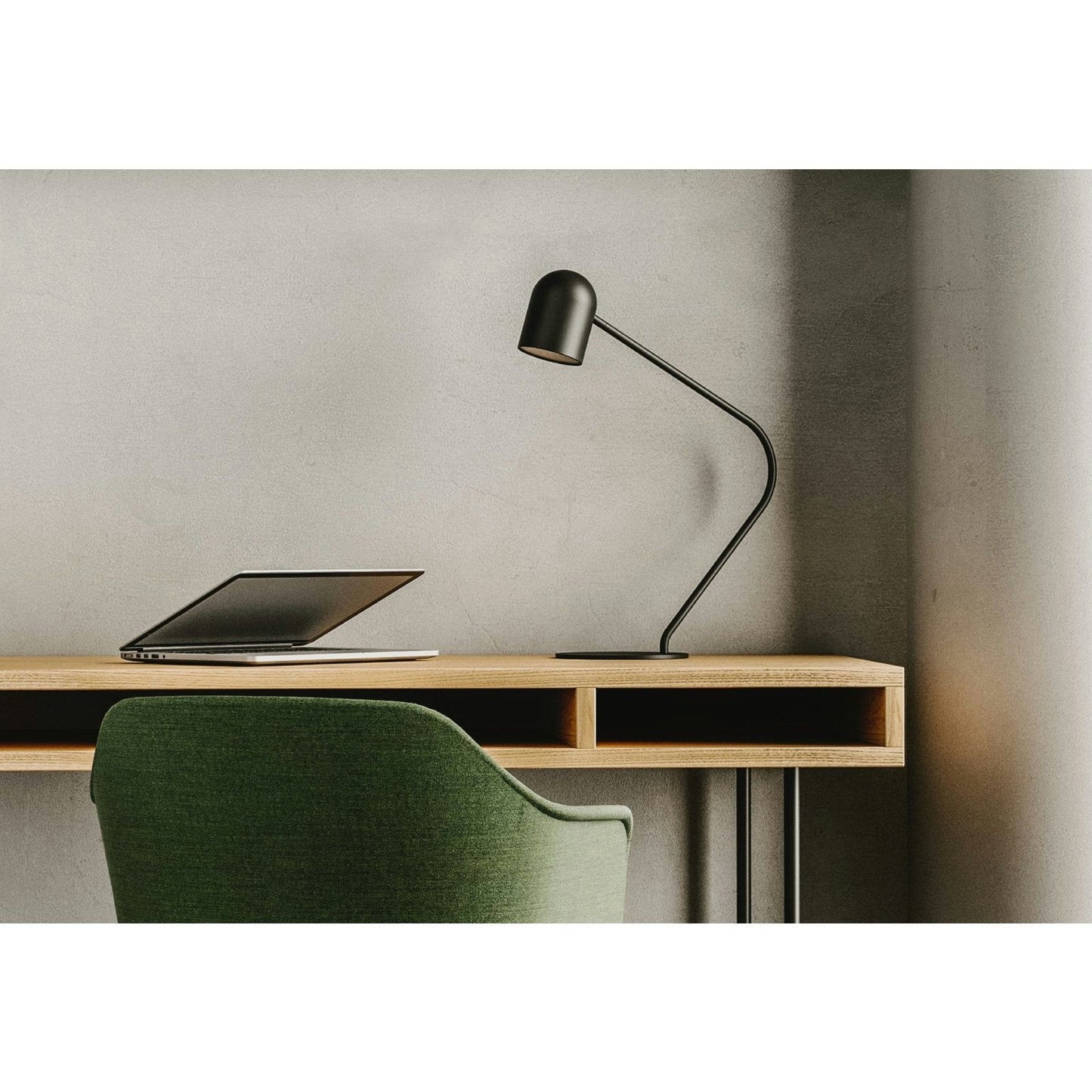 Una configuración de escritorio minimalista incluye un escritorio de madera, una computadora portátil negra y la elegante lámpara de mesa Pipe para una iluminación precisa, combinada con una silla tapizada en verde.
