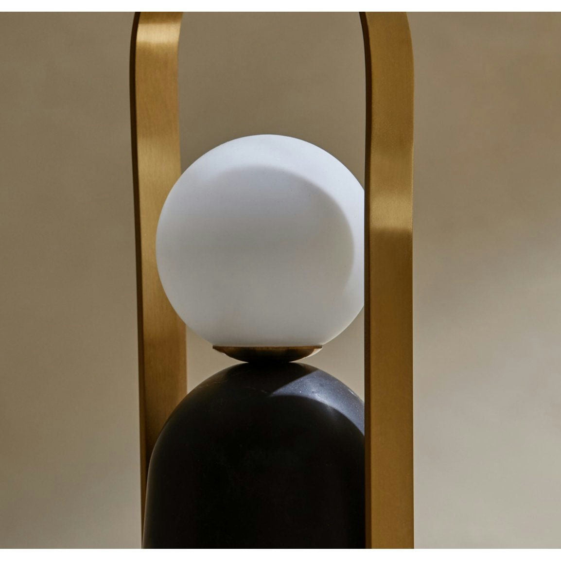La lámpara de mesa Portátil Nano cuenta con una pantalla esférica blanca, una base negra y un marco de arco dorado, todo ello sobre un fondo neutro. Este diseño moderno ofrece iluminación LED regulable adecuada para cualquier entorno.