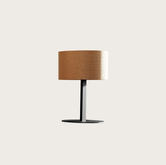 Lámpara de mesa Rems con pantalla beige texturizada y elegante base negra, diseñada para iluminación ambiental, aislada sobre un fondo gris claro.