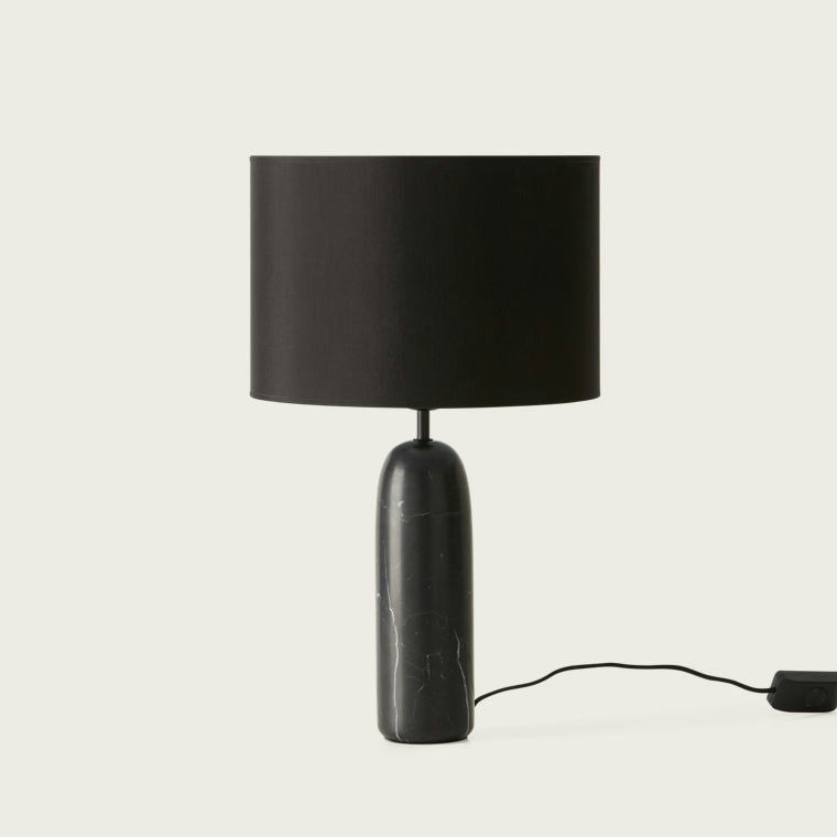 La lámpara de mesa Shin es una lámpara de mesa negra con una base cilíndrica de elegante mármol blanco/negro y una pantalla de tela redonda y ancha. Su discreto cable de alimentación combina diseño clásico y moderno, añadiendo un toque elegante a cualquier estancia.