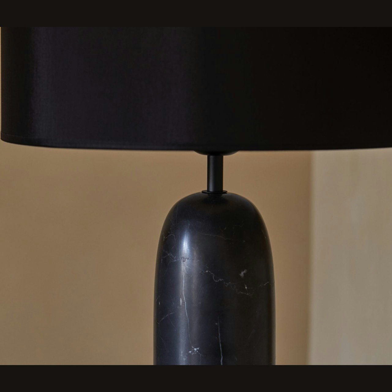 Primer plano de la Lámpara de mesa Shin, con base cilíndrica de mármol negro y pantalla ancha negra, que combina lo clásico y lo moderno sobre un fondo neutro.